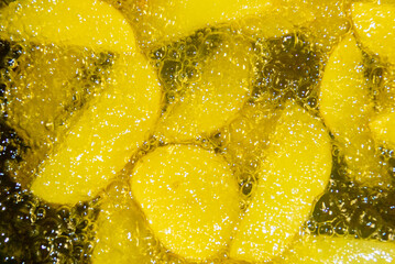 Primer plano de patatas friéndose en aceite caliente. Trozos de patatas rodeadas de burbujas del aceite hirviendo en su proceso de elaboración. French fries.