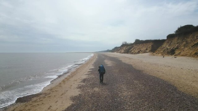 Aerial rear view of a tourist walking along the Kessingland Beach on a cloudy day in Suffolk, England.