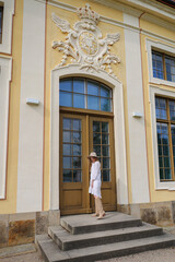 girl in a white dress, beige boots and a beige hat open the door at Moritzburg Castle