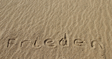 The word PEACE in German. The beautiful word peace is written on the sandy coast. Conceptual inscription on shiny sand and a beautiful seascape background. A word drawn on the beach.