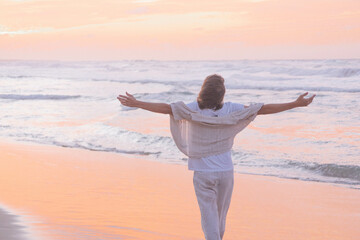Tranquil scene of a person with outstretched arms facing the sea, bathed in the soft hues of a...