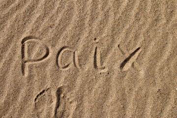 The word PEACE in French. The beautiful word peace is written on the sandy coast. Conceptual inscription on shiny sand and a beautiful seascape background. A word drawn on the beach.