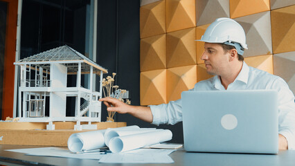 Portrait of professional male caucasian engineer using laptop analysis house construction with...