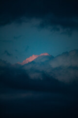 Dramatic view of the dark blue sky with moody dark clouds and small spot of sunlight left on the clouds after sunset.