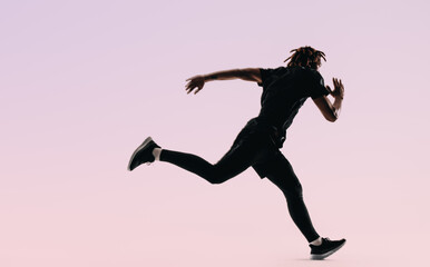 Silhouette of a fit athlete sprinting in a studio with a pink background