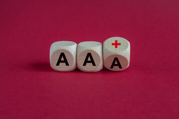 Symbol for a downgrade in a financial rating. Turned a wooden cube and changes the expression AAA to AA plus. Beautiful red background.