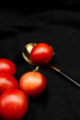 Tomatoes placed on black background. Fresh tomato with a golden spoon for cooking, healthy...