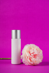 Plastic white tube for cream or lotion. Skin care or sunscreen cosmetic with fake flowers on purple...