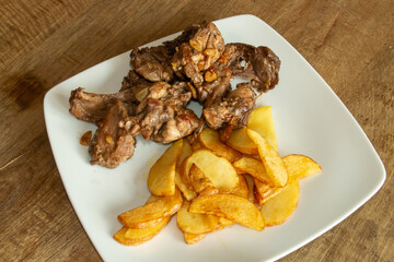 Plato de carne de conejo de caza frito acompañado de patatas fritas. Receta española de carne de conejo de caza frito en aceite de oliva con ajo, laurel, pimienta negra, guindilla y vino blanco.