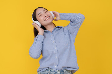 Joyful young woman dancing with headphones on yellow background