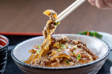 A photo of a delicious Japanese dish, gyudon. The bowl is filled with rice, thinly sliced beef, and...