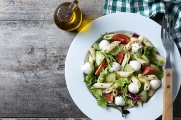 Pasta salad with vegetables and mozzarella cheese on wooden table. Top view. Copy space
