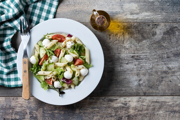Pasta salad with vegetables and mozzarella cheese on wooden table. Top view. Copy space