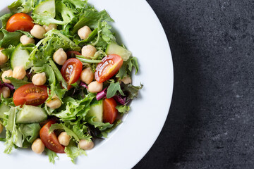 Healthy chickpea salad with tomato,lettuce and cucumber on black slate background