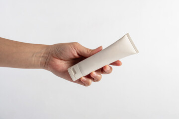 Plastic white tube for cream or lotion. Skin care or sunscreen cosmetic with hand on white background.