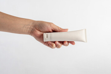 Plastic white tube for cream or lotion. Skin care or sunscreen cosmetic with hand on white background.