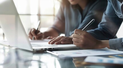 Close up of two asian colleagues working together, have a discussion and using laptop computer at office with financial document on desk