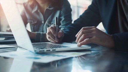 Close up of two asian colleagues working together, have a discussion and using laptop computer at office with financial document on desk