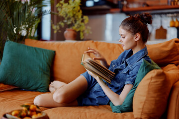 Woman relaxing on an orange couch reading a book in cozy living room setting