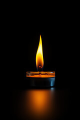 A solitary candle flame casts a warm glow, illuminating its surroundings with a bright, intense light against a stark black background.