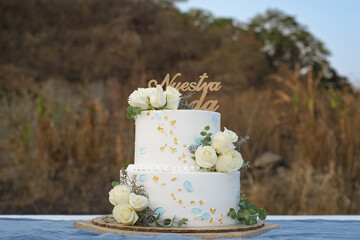 Beautiful wedding cake on an outdoor table. Cake topper with text Our Wedding written in Spanish.