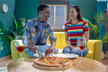 Two female friends celebrating with pizza and wine having fun together at home. High quality photo