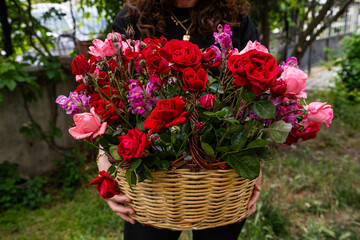 A happy woman holding a basket of red and pink roses in her lap.