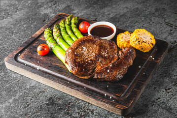 Grilled steak with asparagus, tomato, and sauce on a wooden board