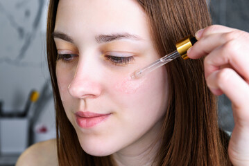 Young woman applying moisturizing facial serum.