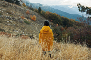 Solo Traveler in Vibrant Yellow Coat Surrounded by Majestic Mountains in a Peaceful Field Landscape...