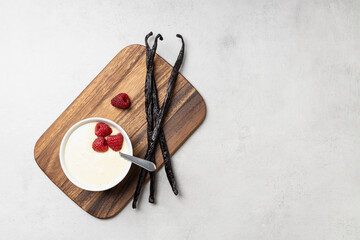 Vanilla pudding with raspberries in white bowl.