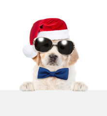 Cute Golden retriever puppy wearing sunglasses and red santa hat looks above empty white banner....
