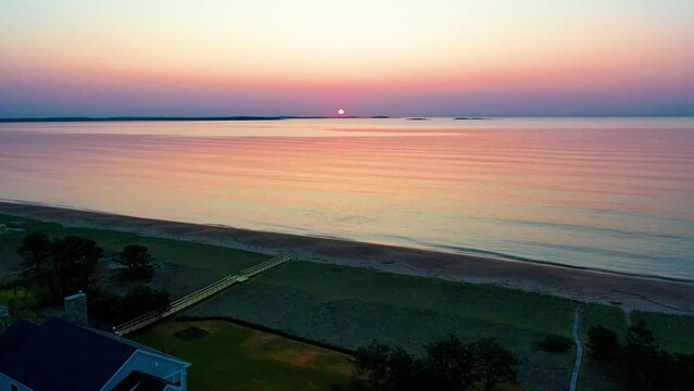 Aerial Drone View of Beautiful Beach Sunrise in Saco Maine with Colors Reflecting off Ocean Waves and Vacation Homes Along the New England Atlantic Coastline. Colorful Golder Hour Sky and Sea Water