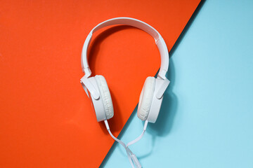 White, full-size wired headphones on a blue-orange background.