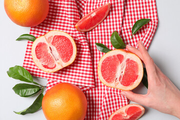 Whole and sliced grapefruits on towel and female hand on white background, top view