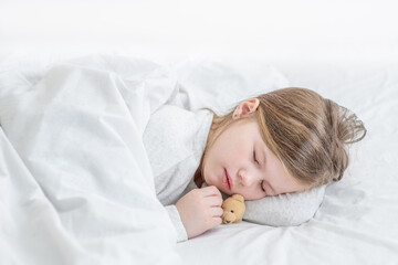 Cute little girl sleeps with toy bear on the bed at home