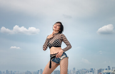 A female hip hop dancer in a snakeskin costume is dancing happily at the top of a high-rise...