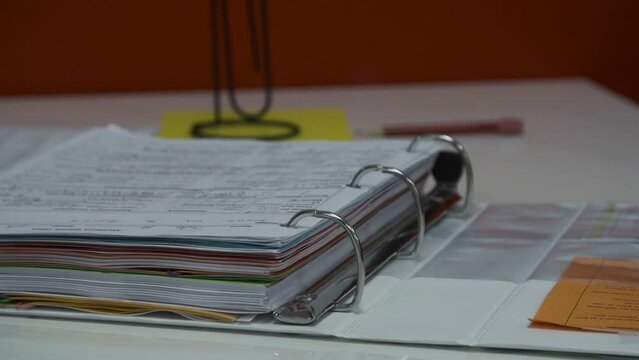 Close up footage of a male hand opening a three ring binder full of educational papers on the desk