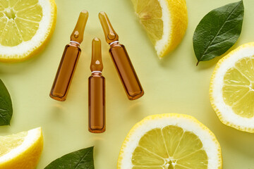 Vitamin C brown ampoules for injection with fresh lemon slices on yellow background. Top view.
