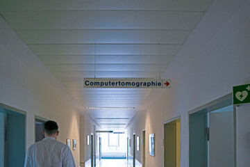 Medicine Concepts. Rear View of Doctor Walking in Hallway For Examining Medical Report of Patient While Passing Computer Tomograph Laboratory in German Hospital Corridor.