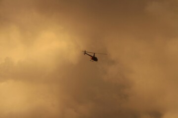 Low angle shot of a helicopter flies through a golden sunset sky