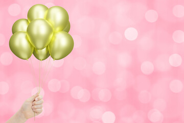 Female hand holding bunch of shiny golden or yellow balloons on blurred pink background. Empty space for text