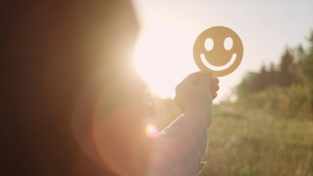 Selective focus of woman holding yellow happy smile face on background amazing warm sunset or sunrise, good feedback rating and positive customer review, satisfaction survey, mental health assessment