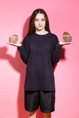 One Winsome Smiling Teenager Girl in Black Shirt Posing with Coconuts Placed in Plastic Containers On hands Indoors Against Pink.