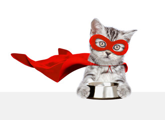 Cute kitten wearing superhero costume holds empty bowl above empty white banner. Isolated on white background