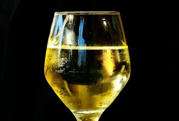 Glass of white wine displayed on a black surface.