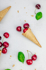 Ripe sweet cherries in waffle cones on light stone concrete background. Flat lay, vintage napkin