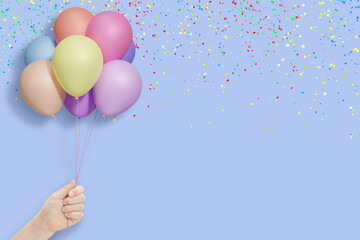 Female hand holds bunch of colorful balloons on blue background with confetti. Empty space for text