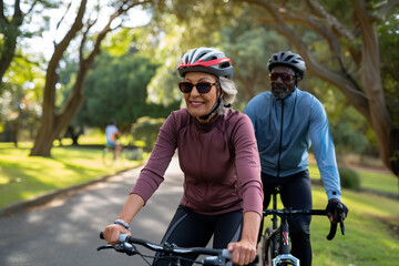 Obraz premium Happy middle-aged couple cycling together in a park, enjoying a sunny day and staying active.