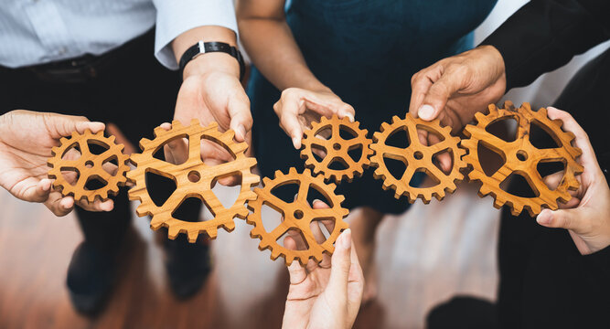 Office worker holding cog wheel as unity and teamwork in corporate workplace concept. Diverse colleague business people showing symbol of visionary system and mechanism for business success. Concord